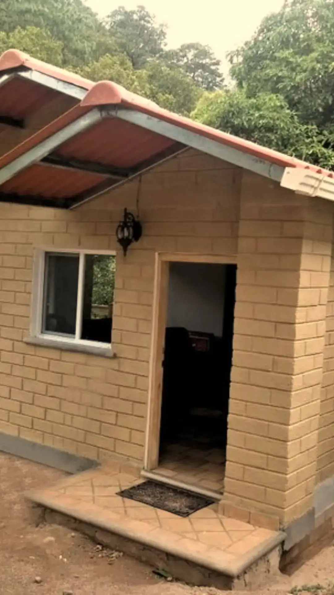 Casa de adobe sencilla de una planta, con la pared de tierra a la vista, cubierta de teja y alero amplio