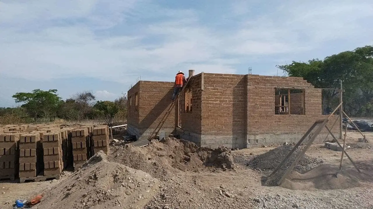 Obra en construcción con bloques de concreto apilados y un trabajador levantando pared