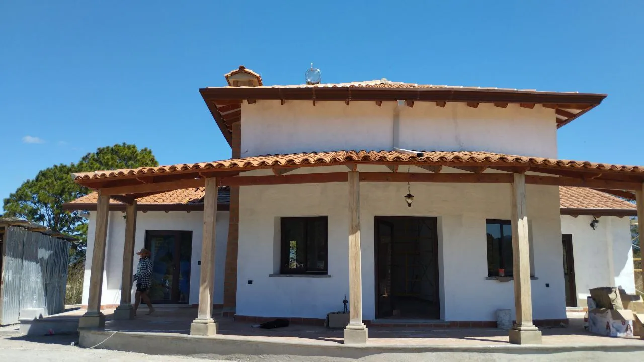 Vivienda rural hondureña de cubierta de teja de barro sobre estructura de madera, con el paisaje del valle al fondo