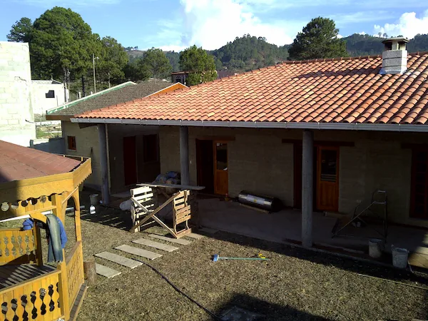 Vivienda ecológica de Ecomobilia con cubierta de teja, corredor y vegetación del sitio alrededor