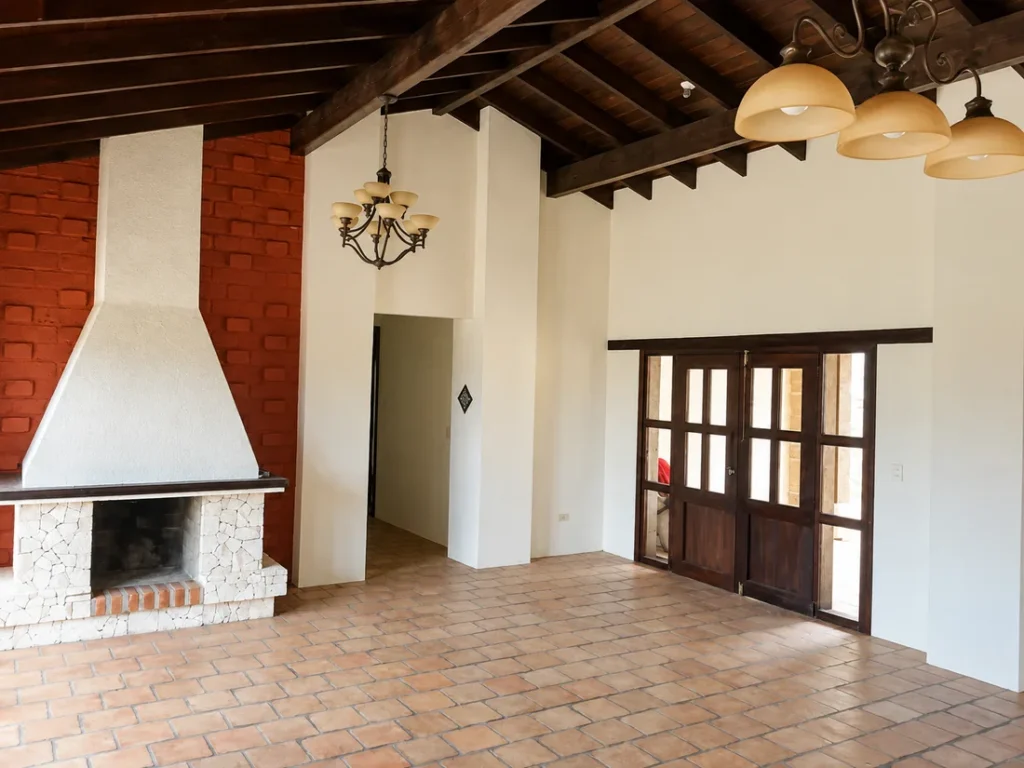 Sala con chimenea de ladrillo, campana blanca, vigas de madera y piso de teja